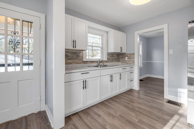 kitchen with visible vents, decorative backsplash, white cabinets, light wood-type flooring, and a sink