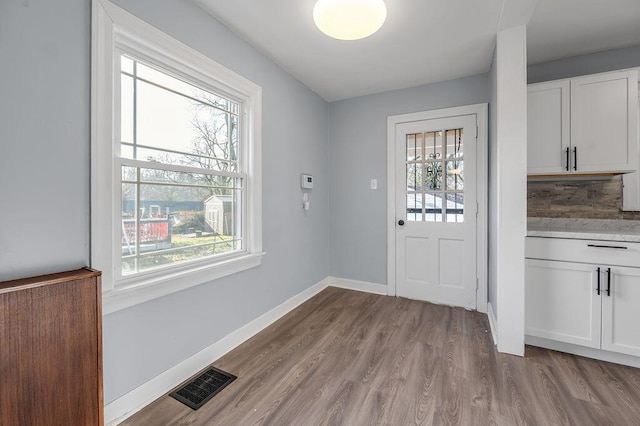 doorway to outside with light wood finished floors, baseboards, and visible vents