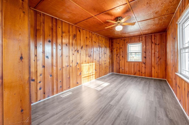 empty room with wooden walls, visible vents, a ceiling fan, wood ceiling, and wood finished floors