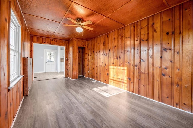 spare room with baseboards, a ceiling fan, wooden ceiling, wood finished floors, and wood walls