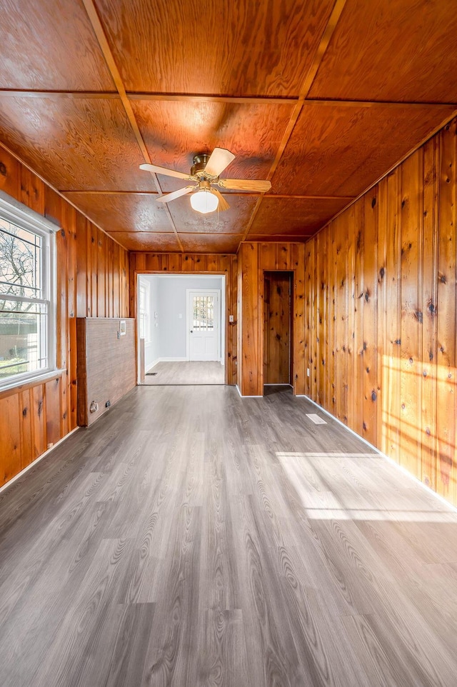 unfurnished living room with wood ceiling, ceiling fan, wooden walls, and wood finished floors