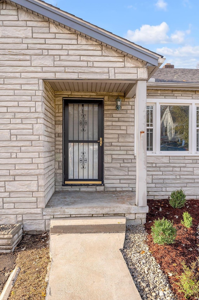 entrance to property featuring stone siding and roof with shingles