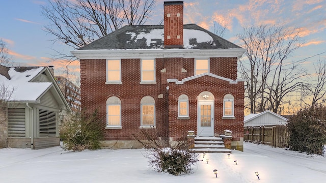 view of front facade with brick siding, fence, a chimney, and roof with shingles