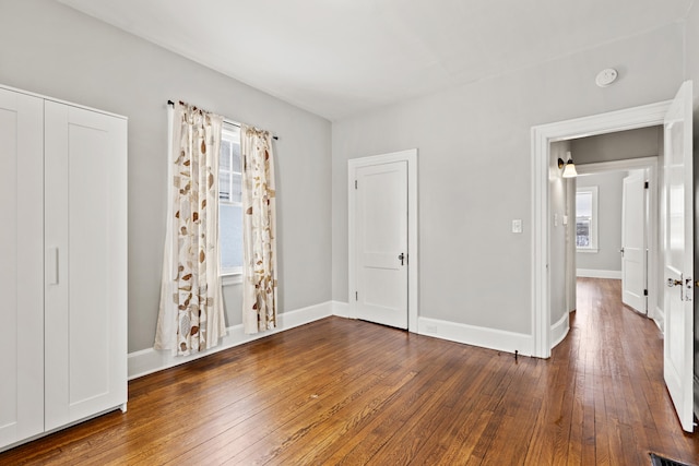 unfurnished bedroom featuring dark wood-style floors, multiple windows, and baseboards