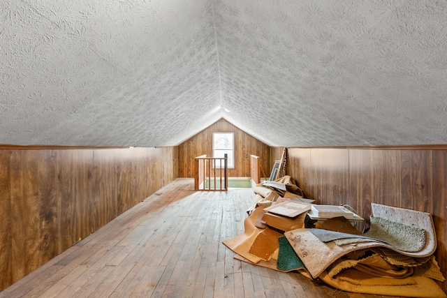 bonus room featuring light wood finished floors, vaulted ceiling, a textured ceiling, and wood walls