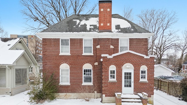 view of front facade with brick siding, a chimney, a shingled roof, and fence