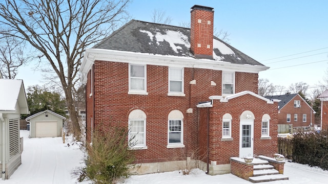 view of front facade with a shingled roof, a detached garage, a chimney, an outdoor structure, and brick siding