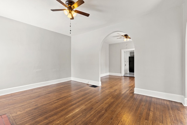 unfurnished room with visible vents, arched walkways, baseboards, dark wood-style floors, and ceiling fan