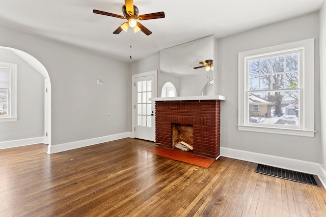 unfurnished living room featuring baseboards, visible vents, dark wood finished floors, arched walkways, and a fireplace