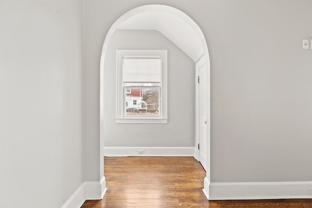 hall featuring baseboards, arched walkways, and wood finished floors