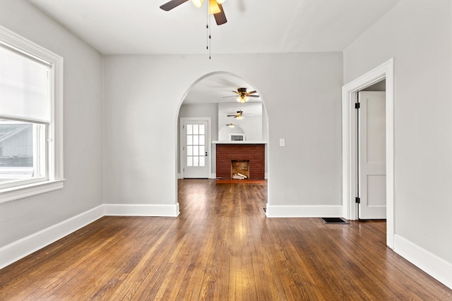 unfurnished room featuring dark wood-style floors, ceiling fan, a fireplace, and baseboards