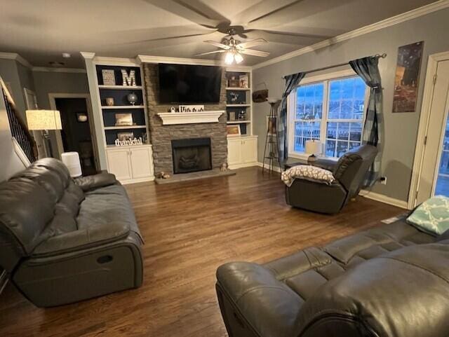 living area featuring baseboards, dark wood finished floors, a ceiling fan, ornamental molding, and a fireplace