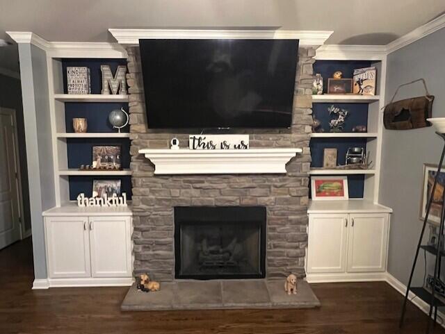 living area with built in shelves, ornamental molding, dark wood finished floors, and a stone fireplace