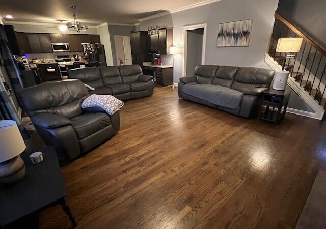 living room featuring dark wood-type flooring, stairway, an inviting chandelier, and crown molding