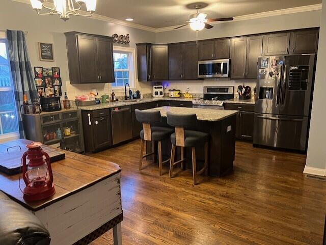 kitchen featuring stainless steel appliances, a kitchen island, a sink, ornamental molding, and dark wood-style floors