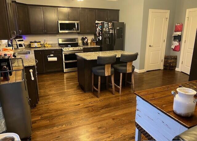 kitchen featuring dark wood-style floors, a center island, a breakfast bar, appliances with stainless steel finishes, and dark brown cabinets