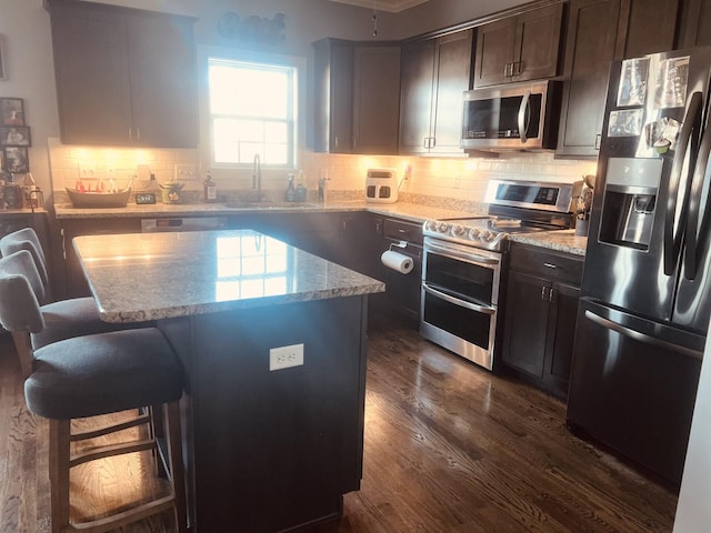 kitchen featuring dark wood-style flooring, appliances with stainless steel finishes, a sink, a kitchen island, and a kitchen bar