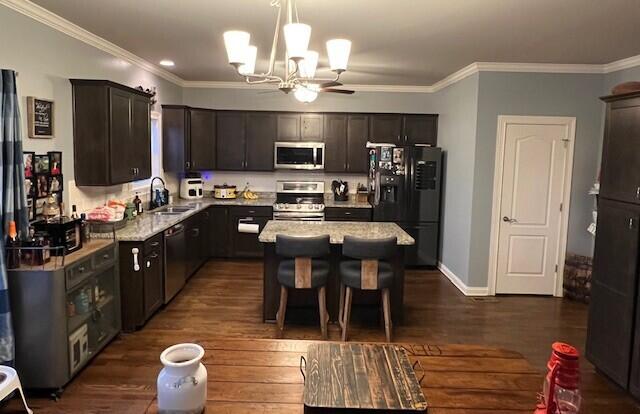 kitchen featuring crown molding, appliances with stainless steel finishes, dark wood-type flooring, dark brown cabinets, and a chandelier