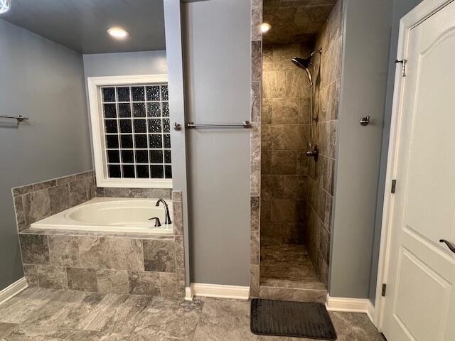 bathroom with a tile shower, baseboards, and a bath