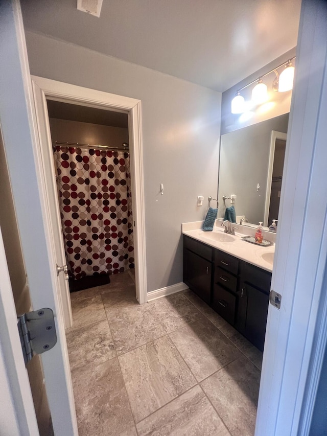 bathroom featuring double vanity, curtained shower, baseboards, and a sink