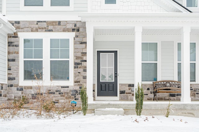 snow covered property entrance with stone siding and covered porch