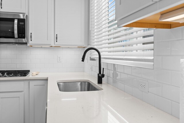 kitchen featuring tasteful backsplash, appliances with stainless steel finishes, white cabinetry, light stone countertops, and baseboards