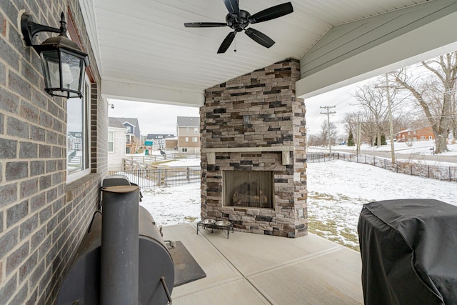 snow covered patio with fence, exterior fireplace, a ceiling fan, and area for grilling