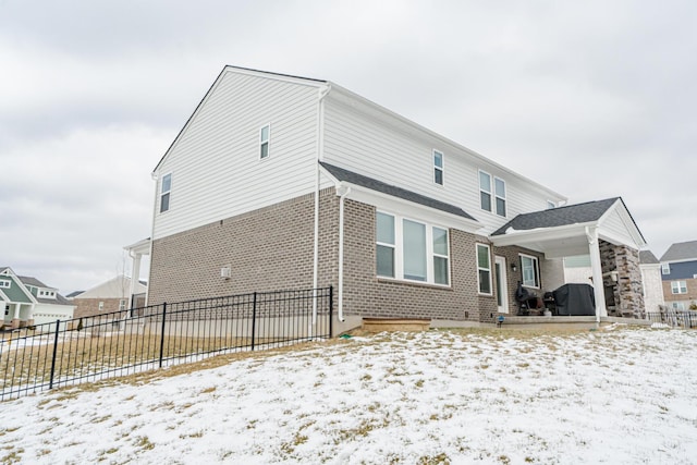 snow covered back of property with brick siding and fence