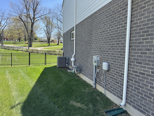 view of side of property featuring a yard, brick siding, central air condition unit, and fence