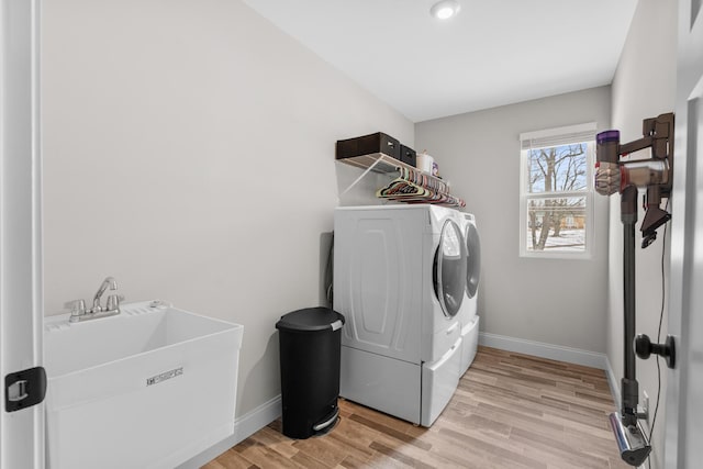 laundry room with laundry area, baseboards, washer and clothes dryer, light wood-style floors, and a sink