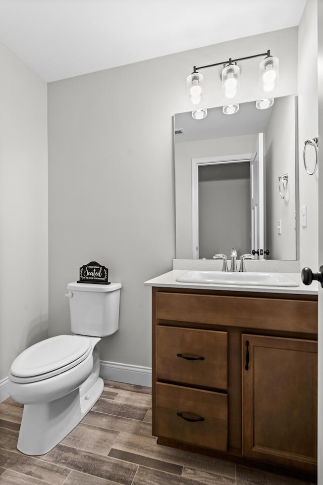 bathroom with toilet, vanity, wood finished floors, and baseboards