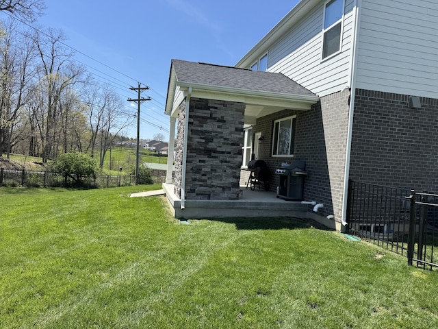 view of property exterior featuring a yard, fence, brick siding, and a shingled roof