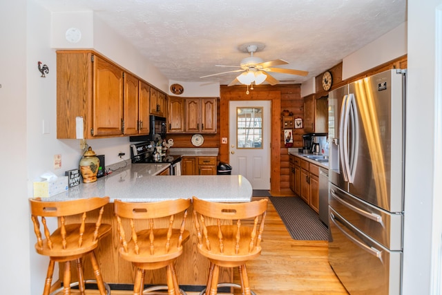 kitchen featuring brown cabinetry, a breakfast bar area, a peninsula, stainless steel appliances, and light wood-style floors