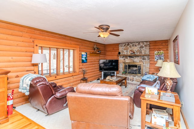 living area featuring a ceiling fan, log walls, wood finished floors, and a stone fireplace