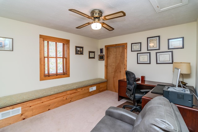 carpeted office featuring a textured ceiling, visible vents, and a ceiling fan