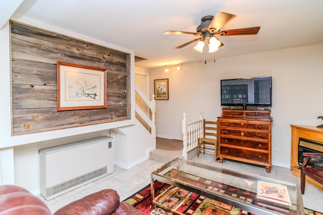 living area featuring a fireplace, heating unit, stairway, a ceiling fan, and baseboards