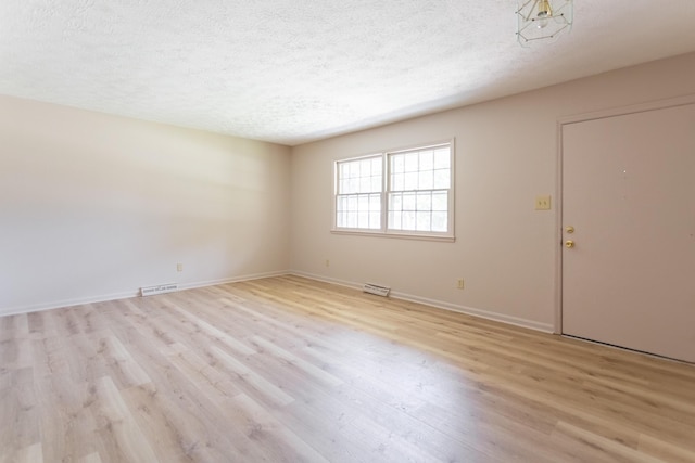 unfurnished room featuring light wood-style floors, visible vents, a textured ceiling, and baseboards