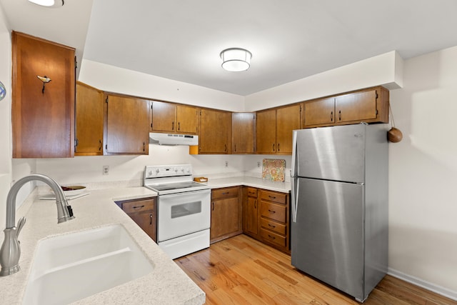 kitchen featuring under cabinet range hood, a sink, light countertops, freestanding refrigerator, and white electric range oven