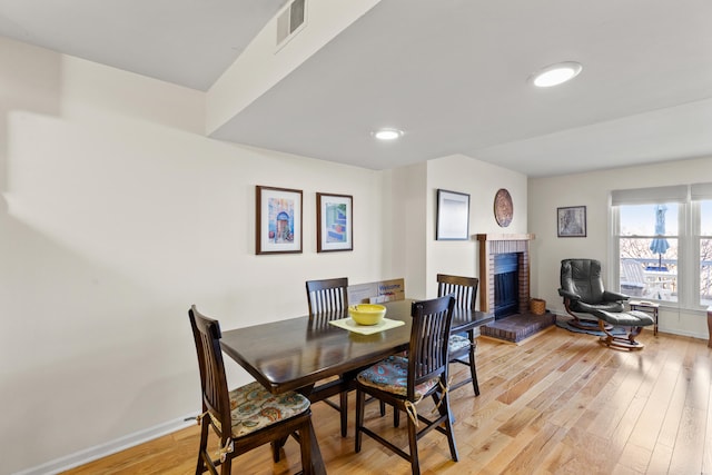 dining space with light wood-style flooring, recessed lighting, visible vents, baseboards, and a brick fireplace