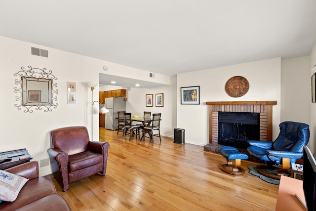 living area with light wood finished floors, baseboards, a fireplace, and visible vents