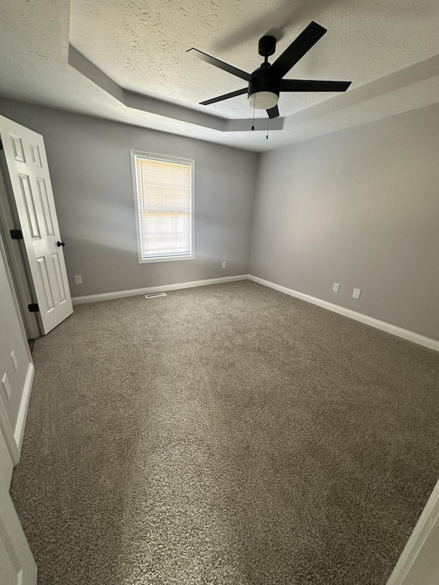 carpeted spare room featuring baseboards, visible vents, ceiling fan, a tray ceiling, and a textured ceiling