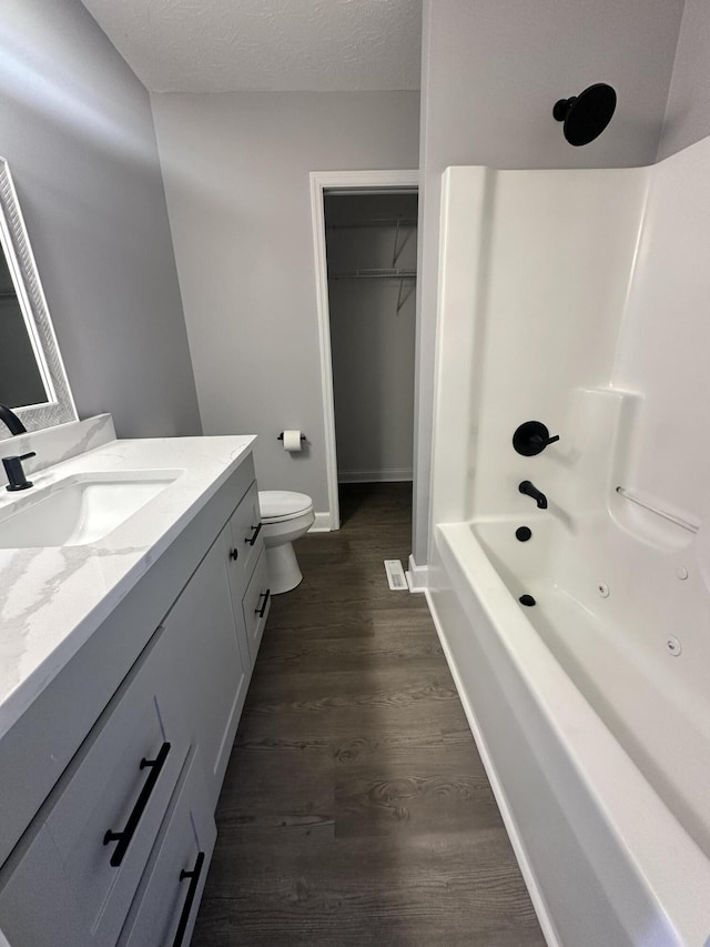 bathroom featuring toilet, wood finished floors, a spacious closet, a textured ceiling, and vanity