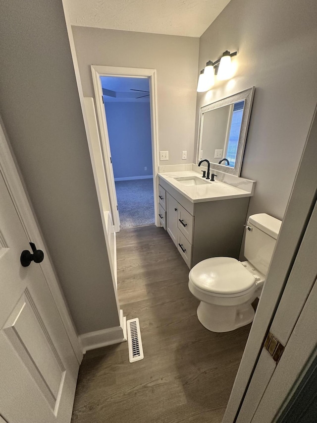 half bathroom featuring visible vents, toilet, vanity, wood finished floors, and baseboards