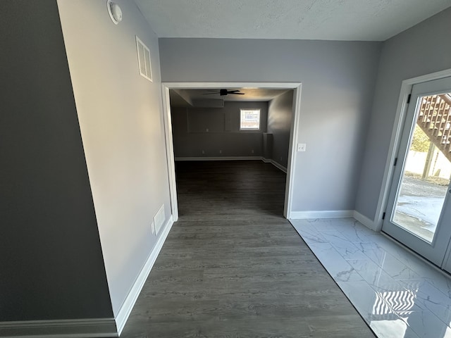 corridor featuring marble finish floor, baseboards, visible vents, and a textured ceiling