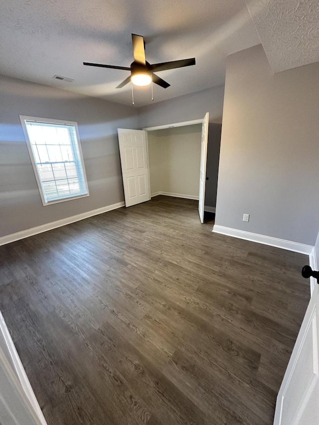 unfurnished bedroom featuring a ceiling fan, a textured ceiling, baseboards, and dark wood-style flooring