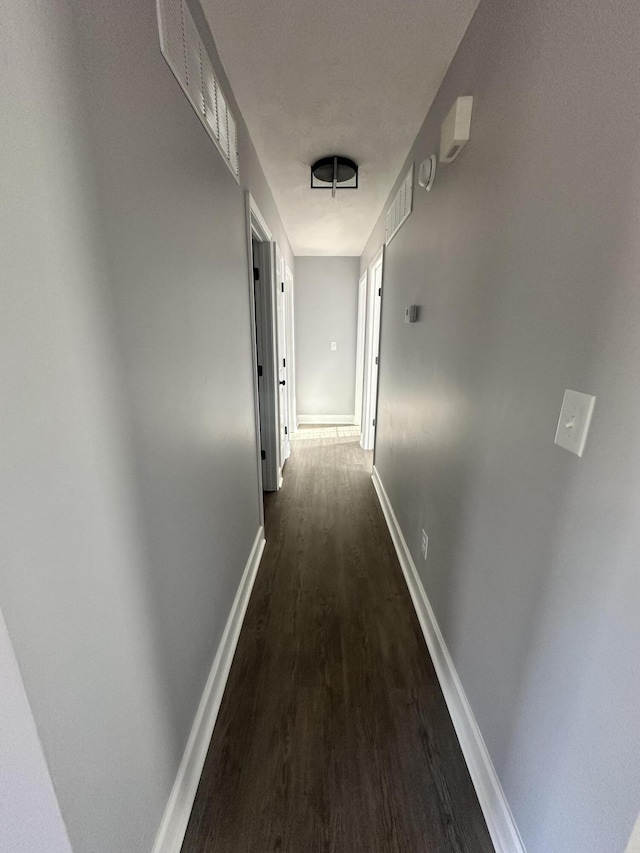 corridor with visible vents, baseboards, and dark wood finished floors