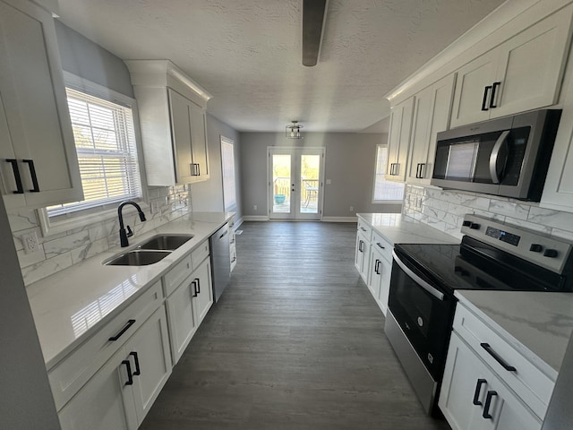 kitchen with light stone counters, dark wood-style flooring, stainless steel appliances, white cabinets, and a sink