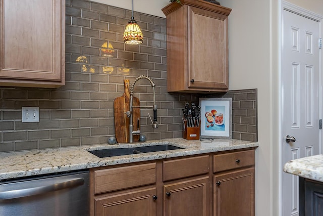 kitchen featuring a sink, hanging light fixtures, stainless steel dishwasher, backsplash, and light stone countertops