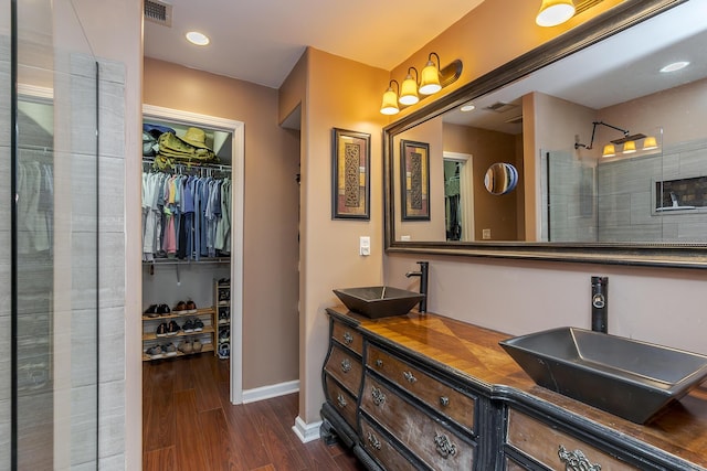 bathroom featuring visible vents, wood finished floors, a tile shower, a walk in closet, and a sink