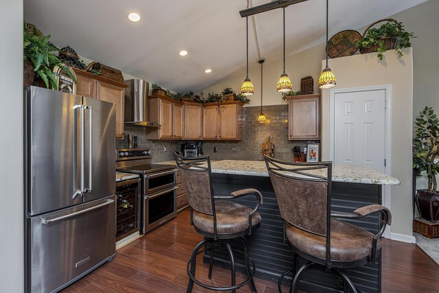 kitchen featuring light stone counters, stainless steel appliances, a kitchen island, wall chimney range hood, and brown cabinets